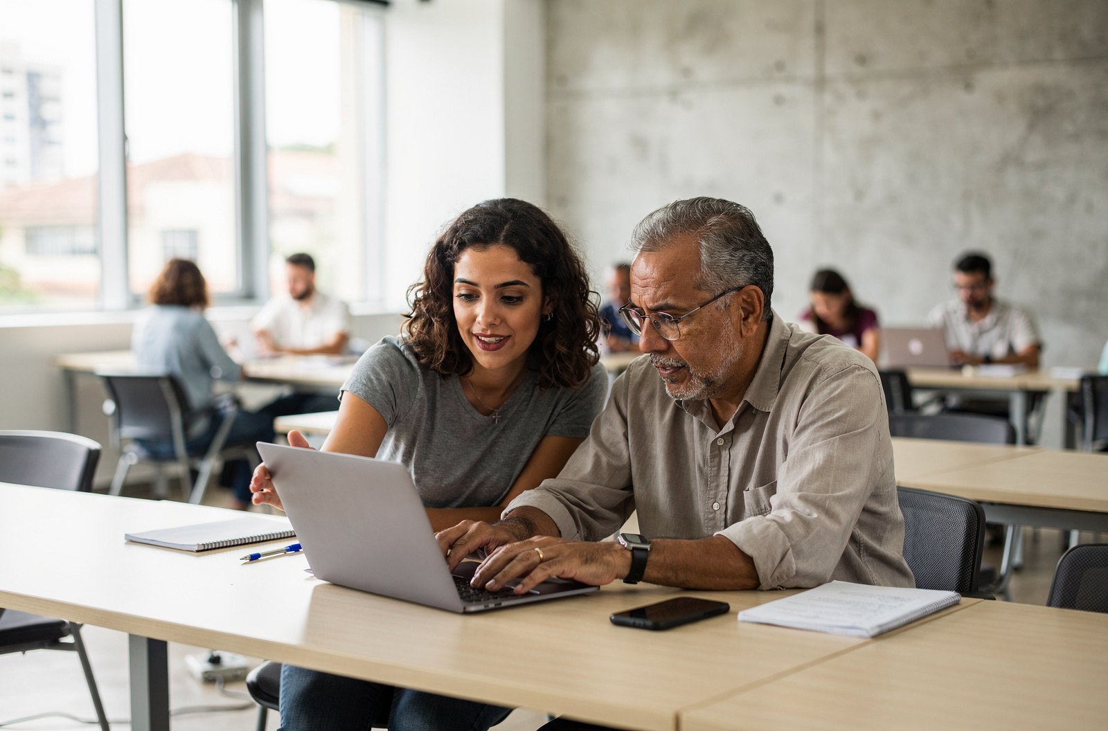 Dois estudantes programam juntos em um notebook, em sala de aula